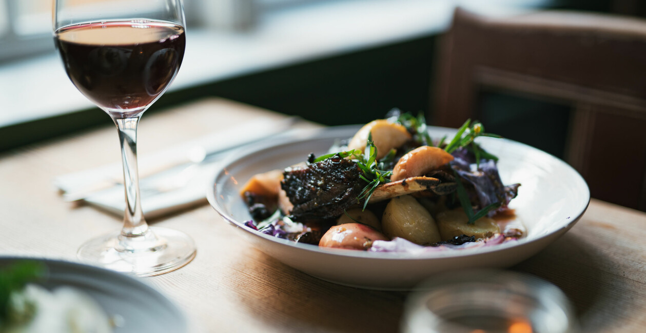I Gunnebo Slottsrestaurang serveras ekologisk mat efter säsong. Foto: Lina Ikse Ett glas rött vin och en tallrik med elegant upplagt kött och grönsaker.