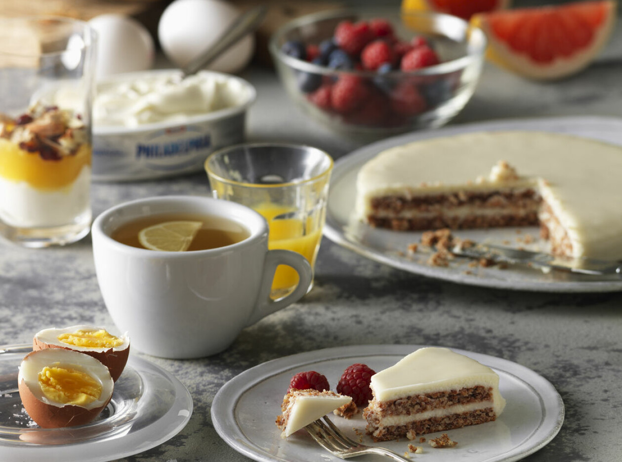 På ett frukostbord med bär, ägg, uppskivad grepefrukt, te och kaffe står ett fat och en tallrik med tårta.