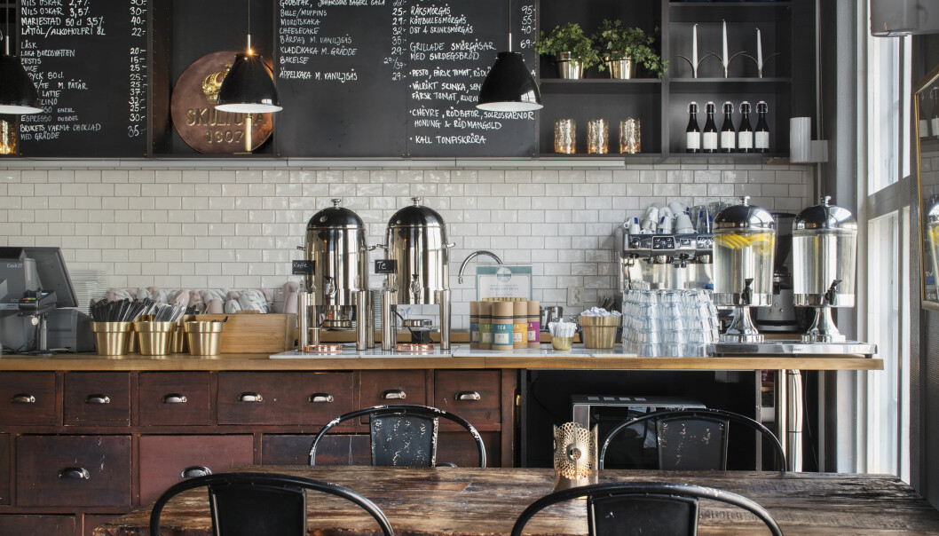 Ett kaffe med vita klinkersväggar, griffeltavlor och ett rustikt träbord på Skultuna Fabriksbutiker.
