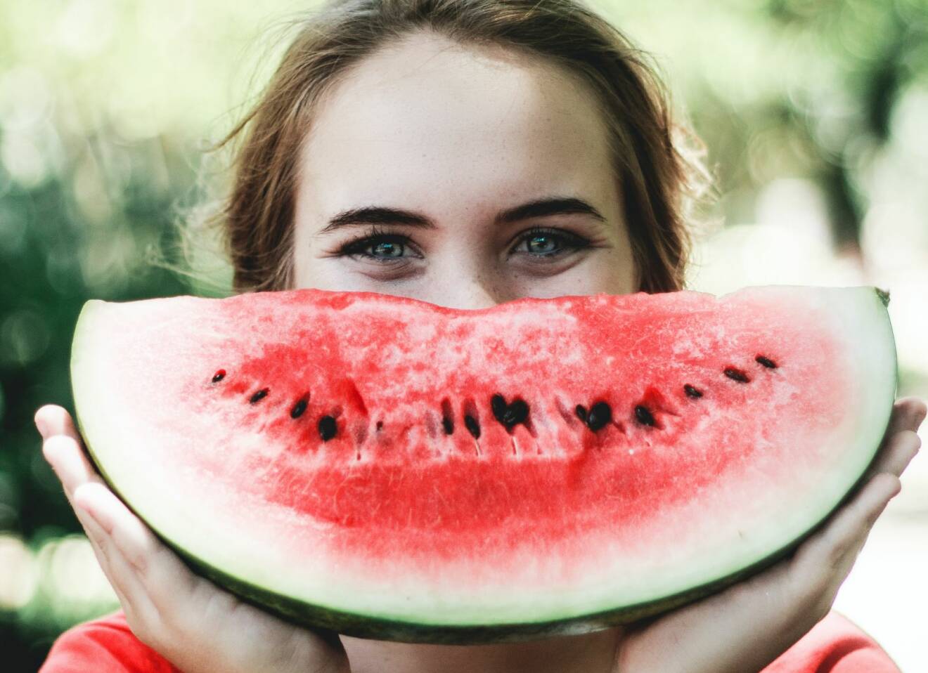 Leende kvinna håller upp en vattenmelon framför ansiktet.