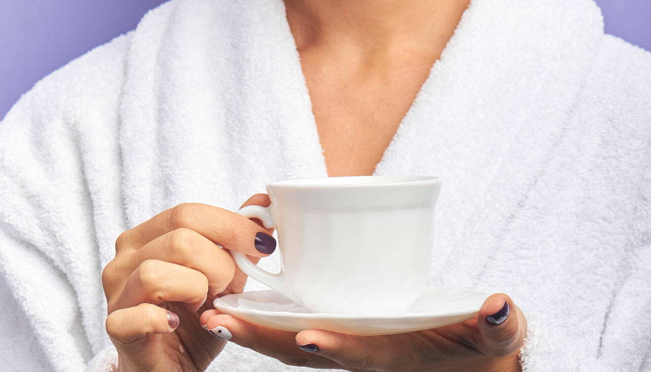 Kvinna i badrock håller i kaffekopp.