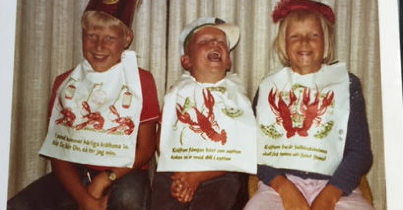 Barnbild på storskrattande Janne mellan två syskon, alla med stora kräfthaklappar.