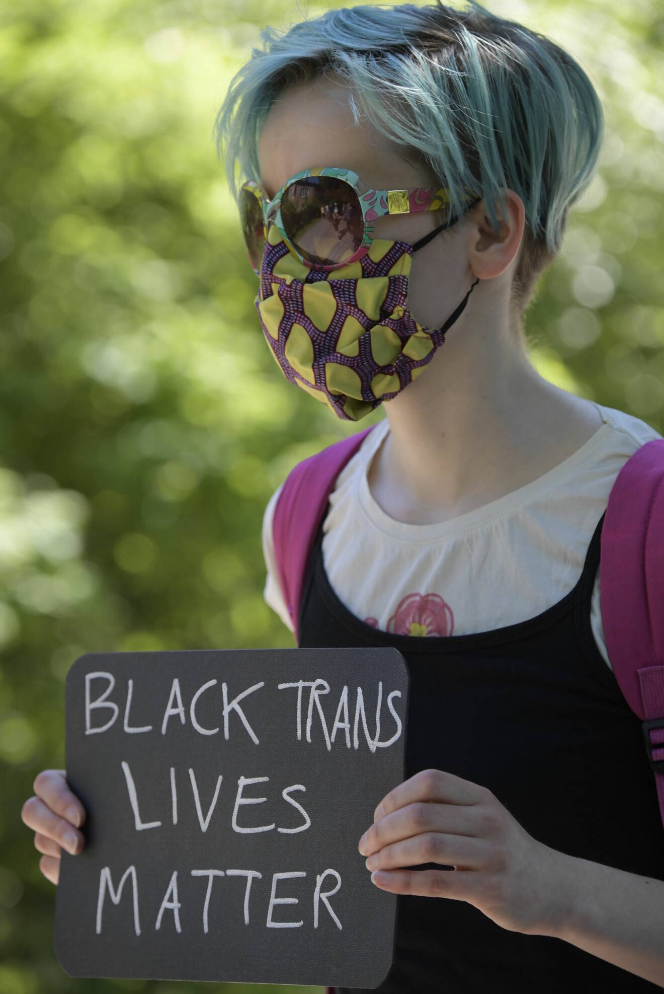En demonstrant med ansiktsmask håller upp skylten "Black trans lives matter".