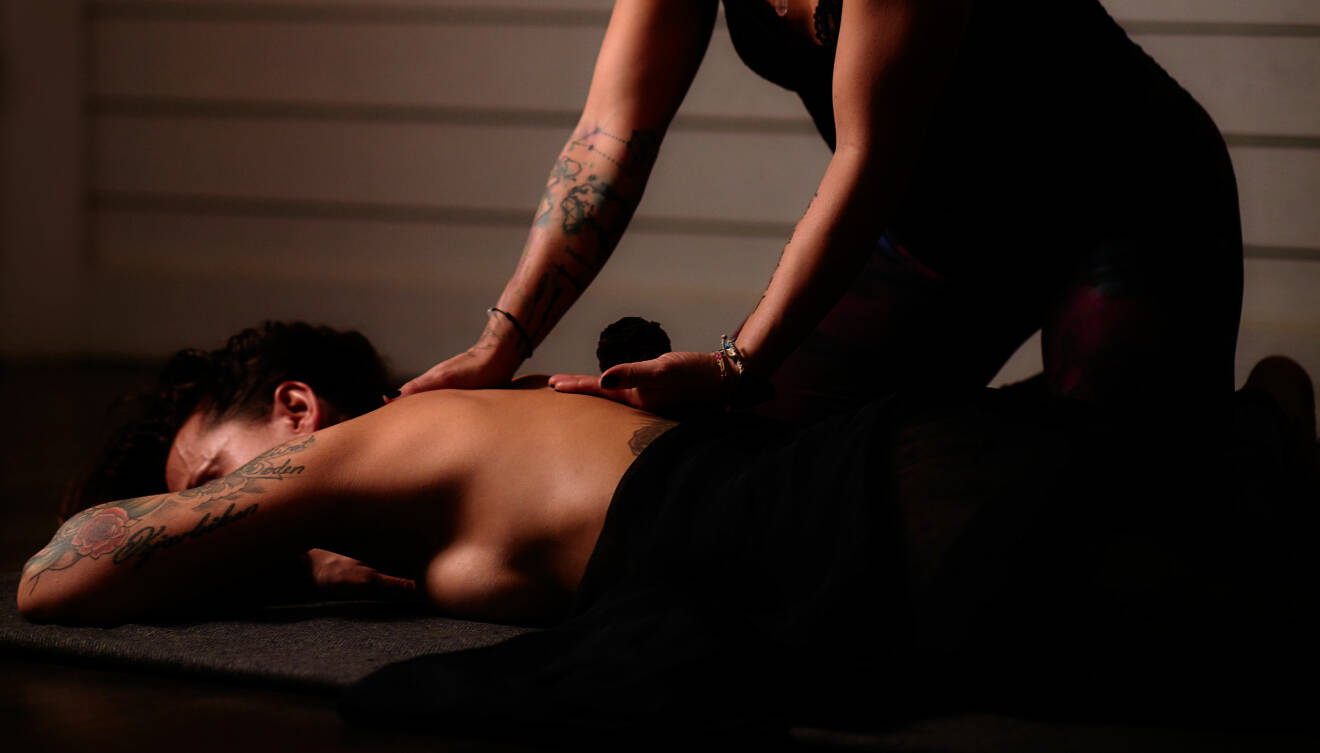En kvinna ligger på mage med en bar rygg. Jaandrée lutar sig över henne och berör ryggen med sina händer.