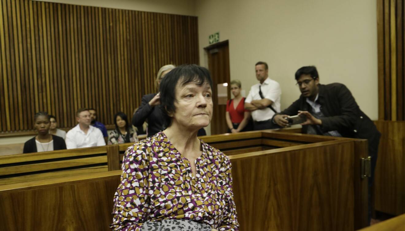 En äldre kvinna i mönstrad blus sitter i en rättegångssal och ser sammanbiten ut.