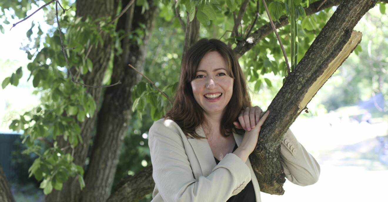 Skådespelaren Sanna Sundqvist står lutad mot ett träd.