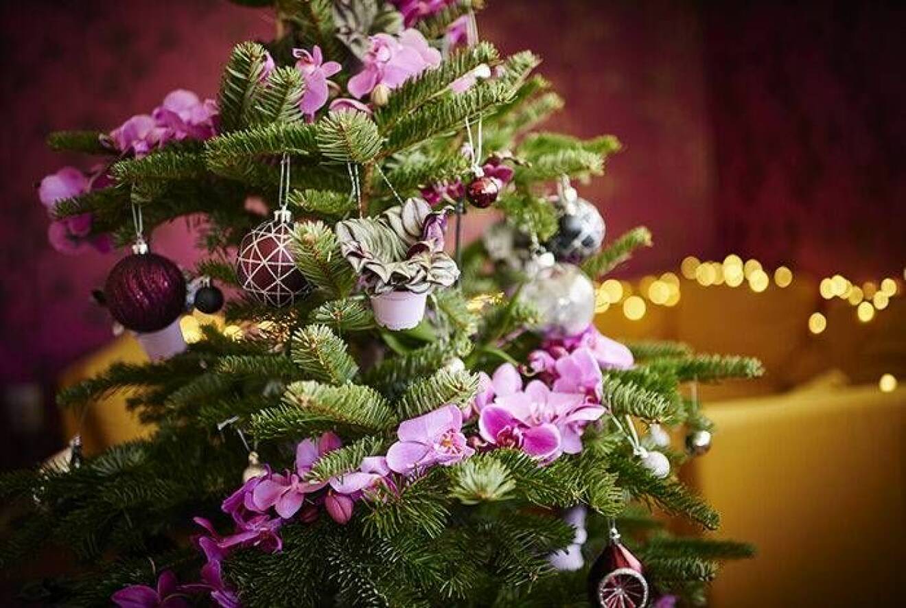 Julgran dekorerad med lila blommor och pynt i matchande färg