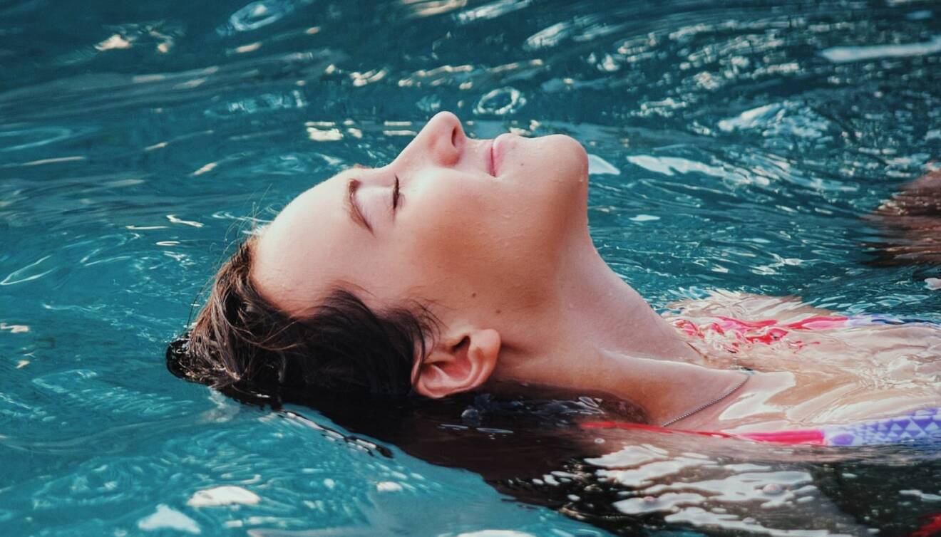 Kvinna njuter av sommaren genom att flyta på ryggen i en pool.