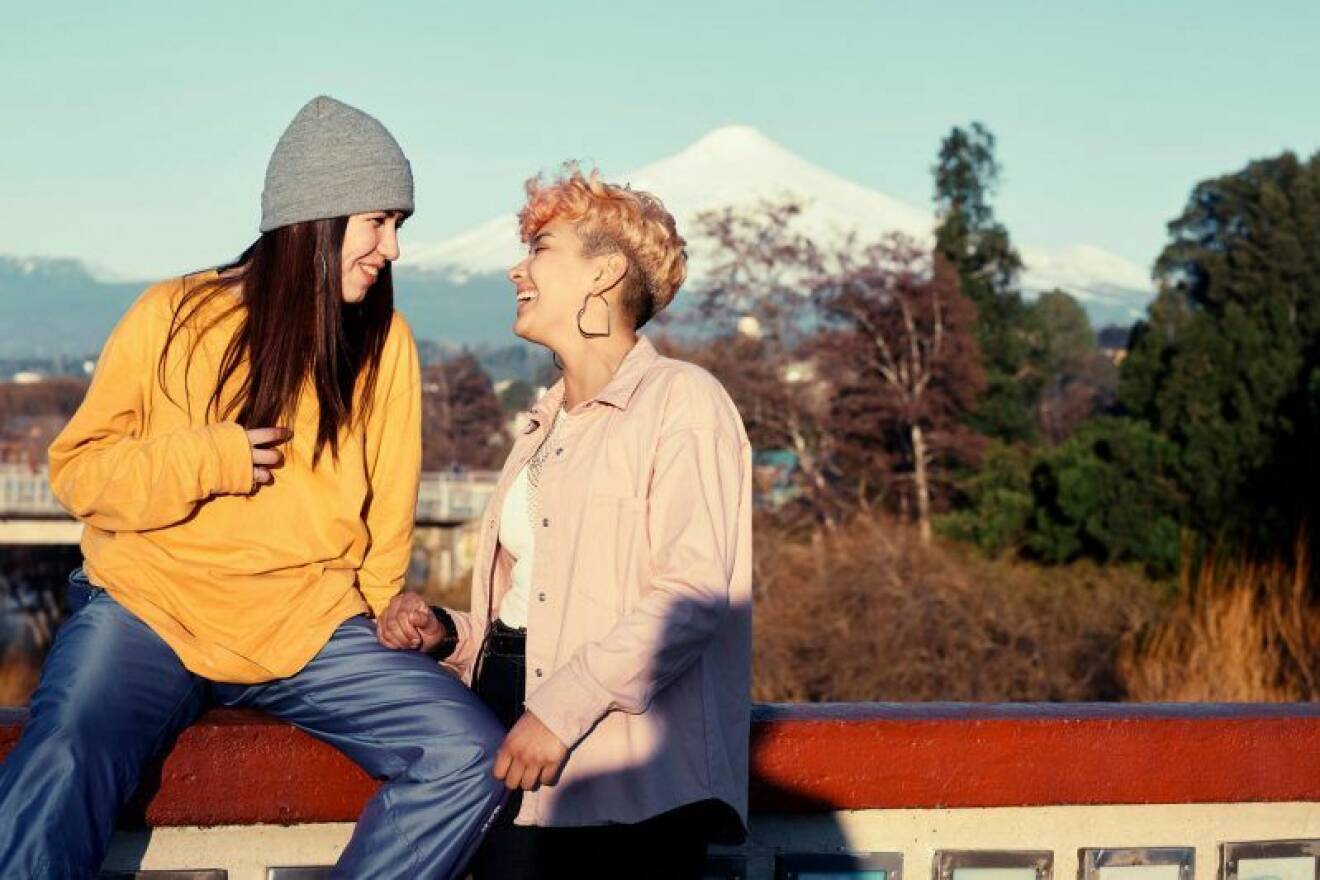 Två kvinnor ler mot varandra med ett berglandskap i bakgrunden.