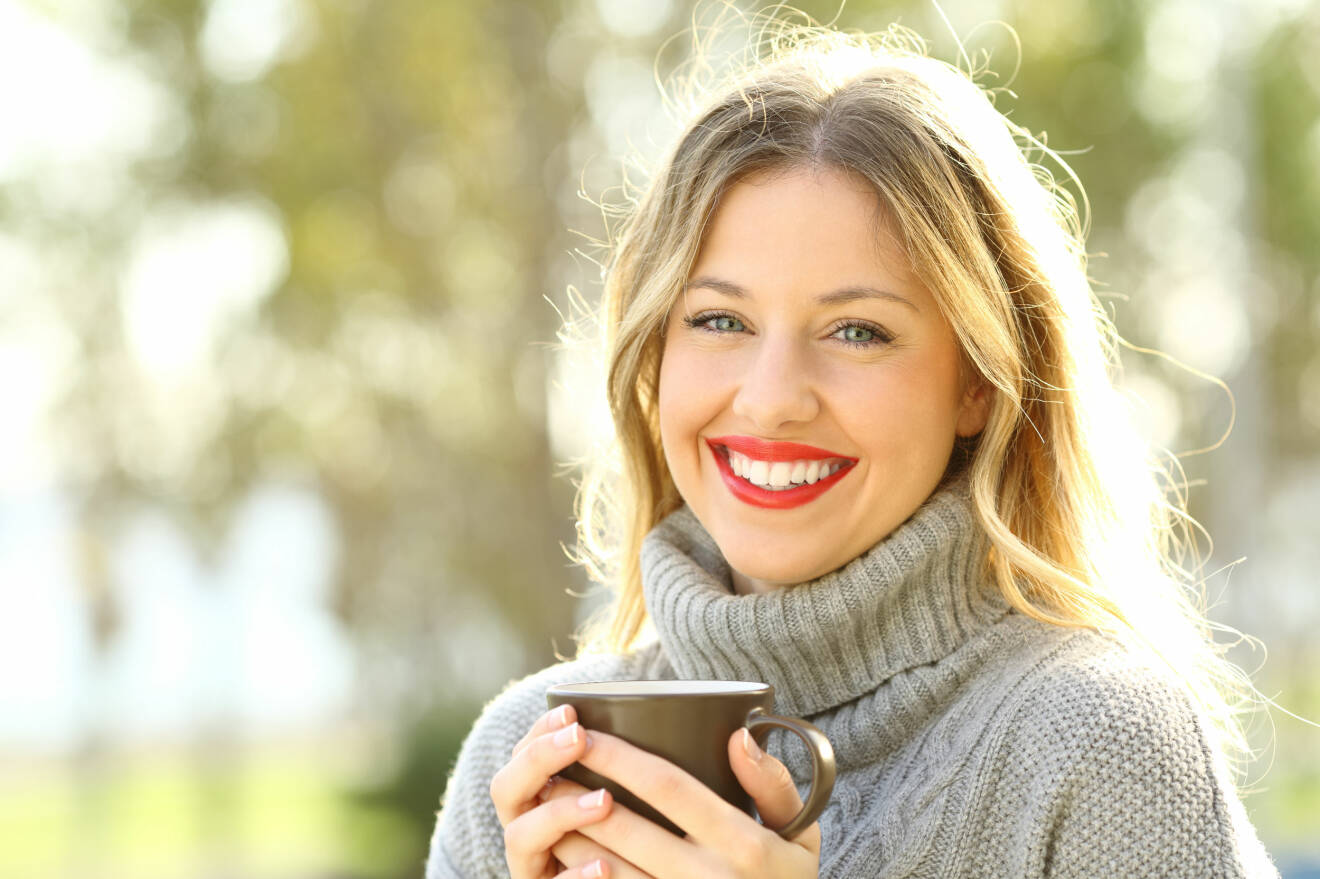 Leende kvinna håller en kopp kaffe i handen.