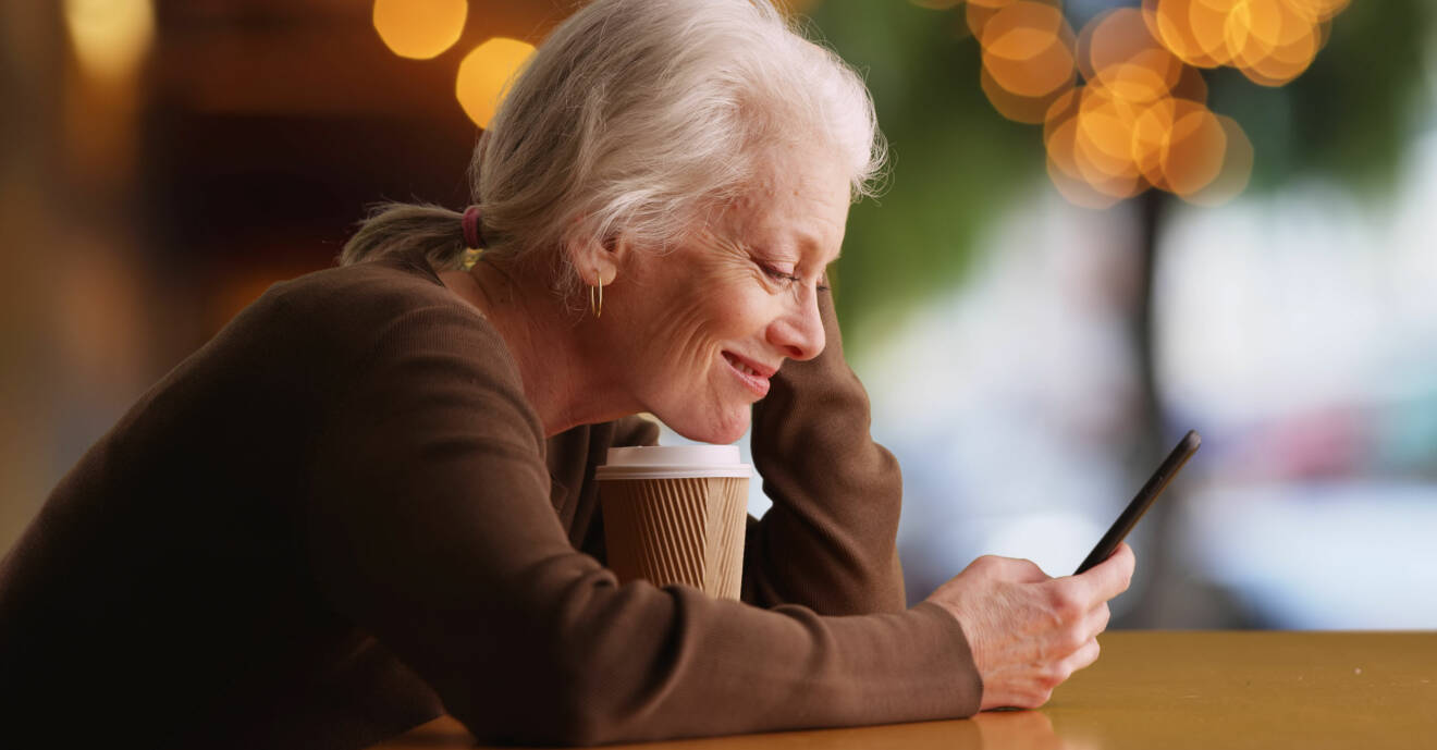 Kvinna Spelar spel på mobilen och dricker kaffe.