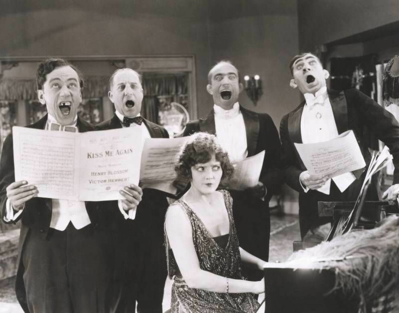 Män sjunger ackompanjerad till kvinna med piano på 20-30-talet.