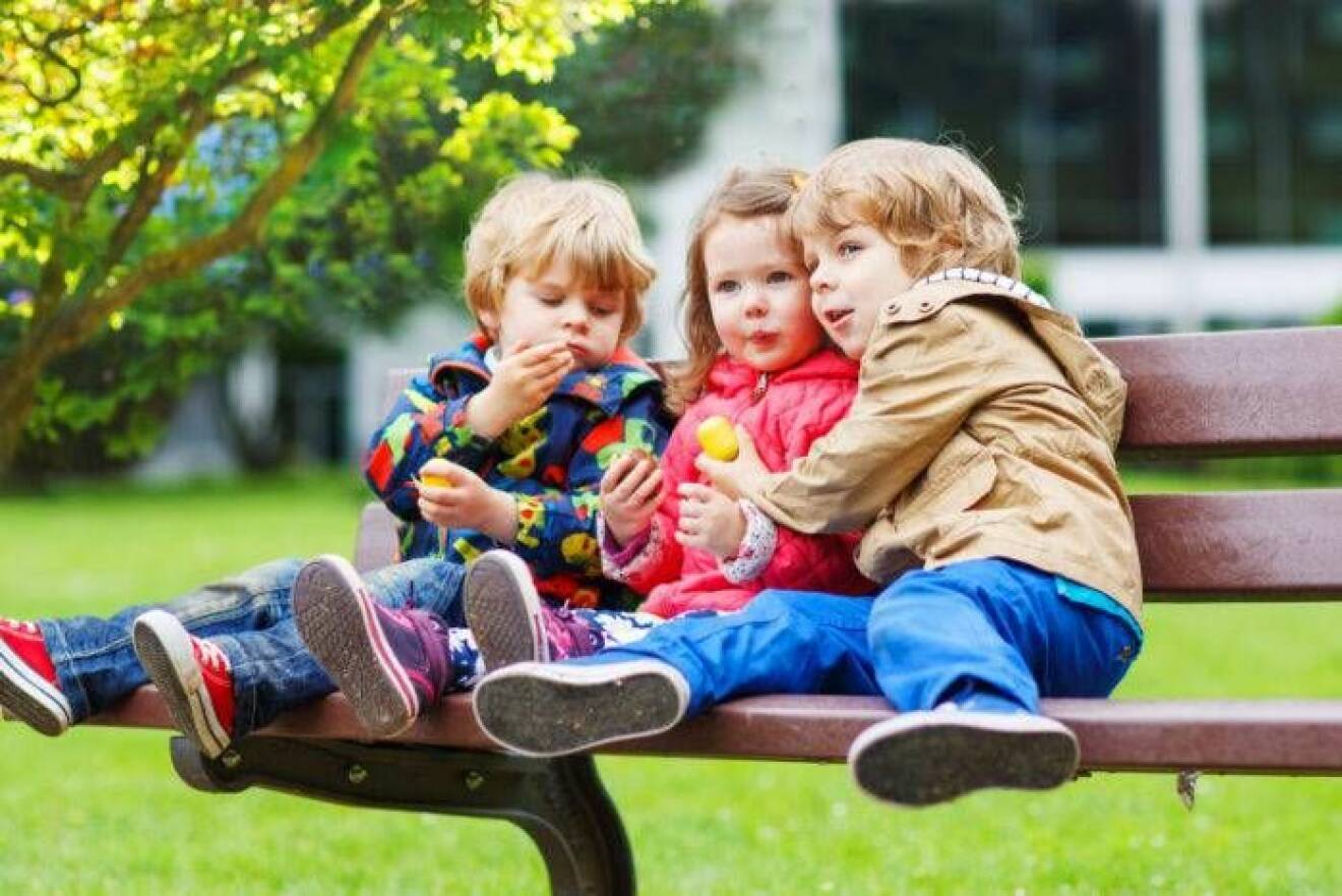 Tre små barn på parkbänk.