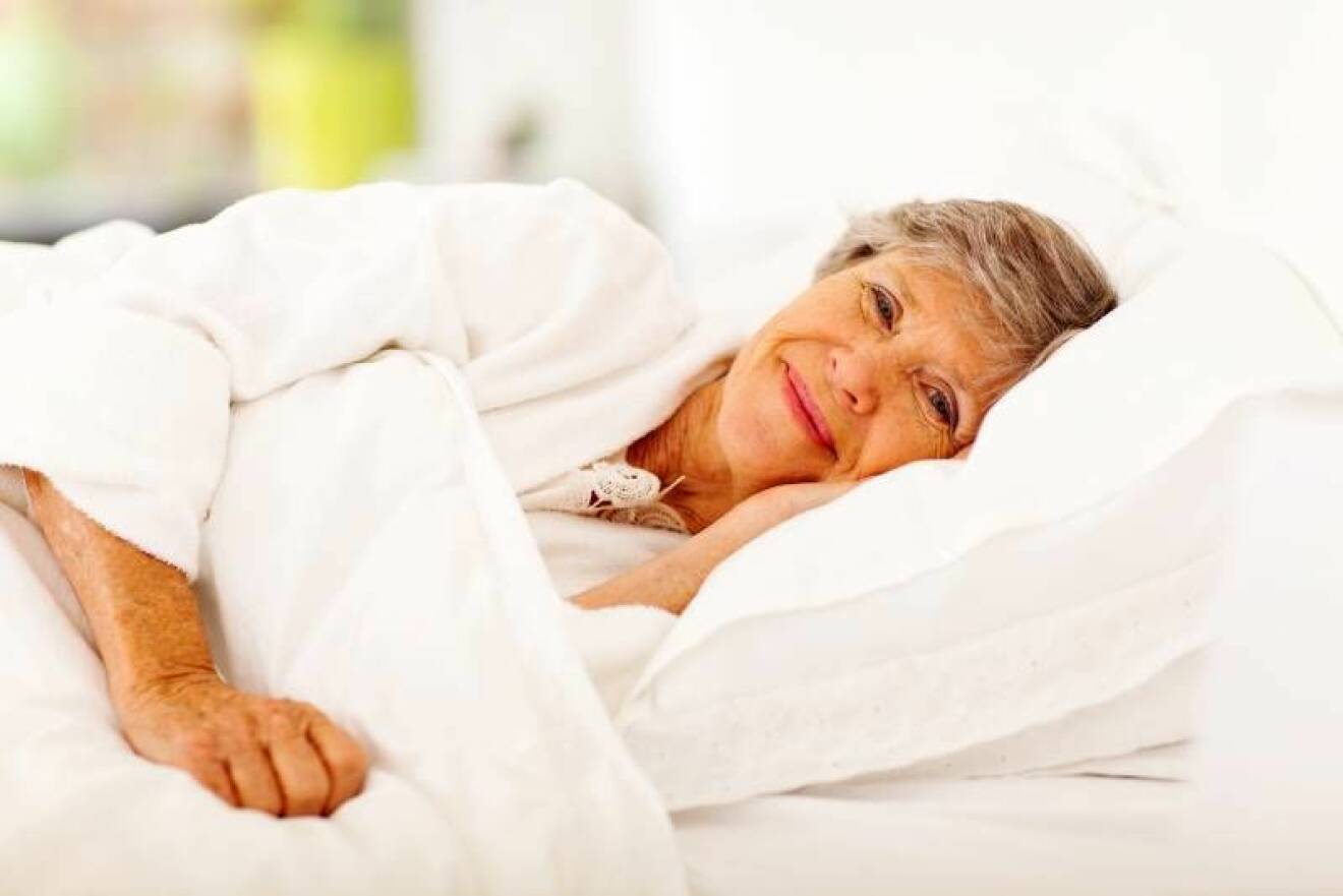 Kvinna ligger i säng och ser glad ut.