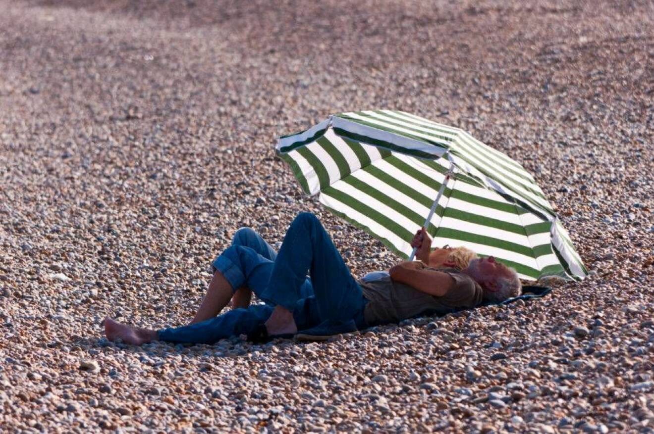 Kvinna och man under parasoll på strand.