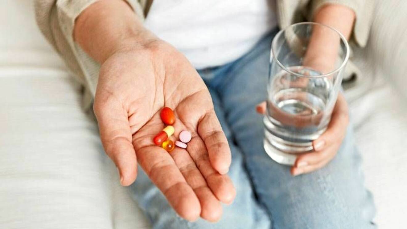 En hand med tabletter och en hand som håller ett glas vatten.