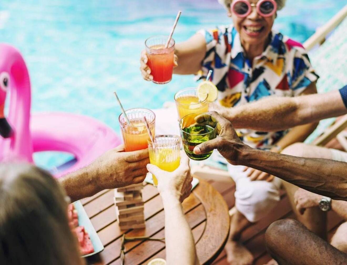 Seniorer skålar i färgglada drinkar vid poolen.