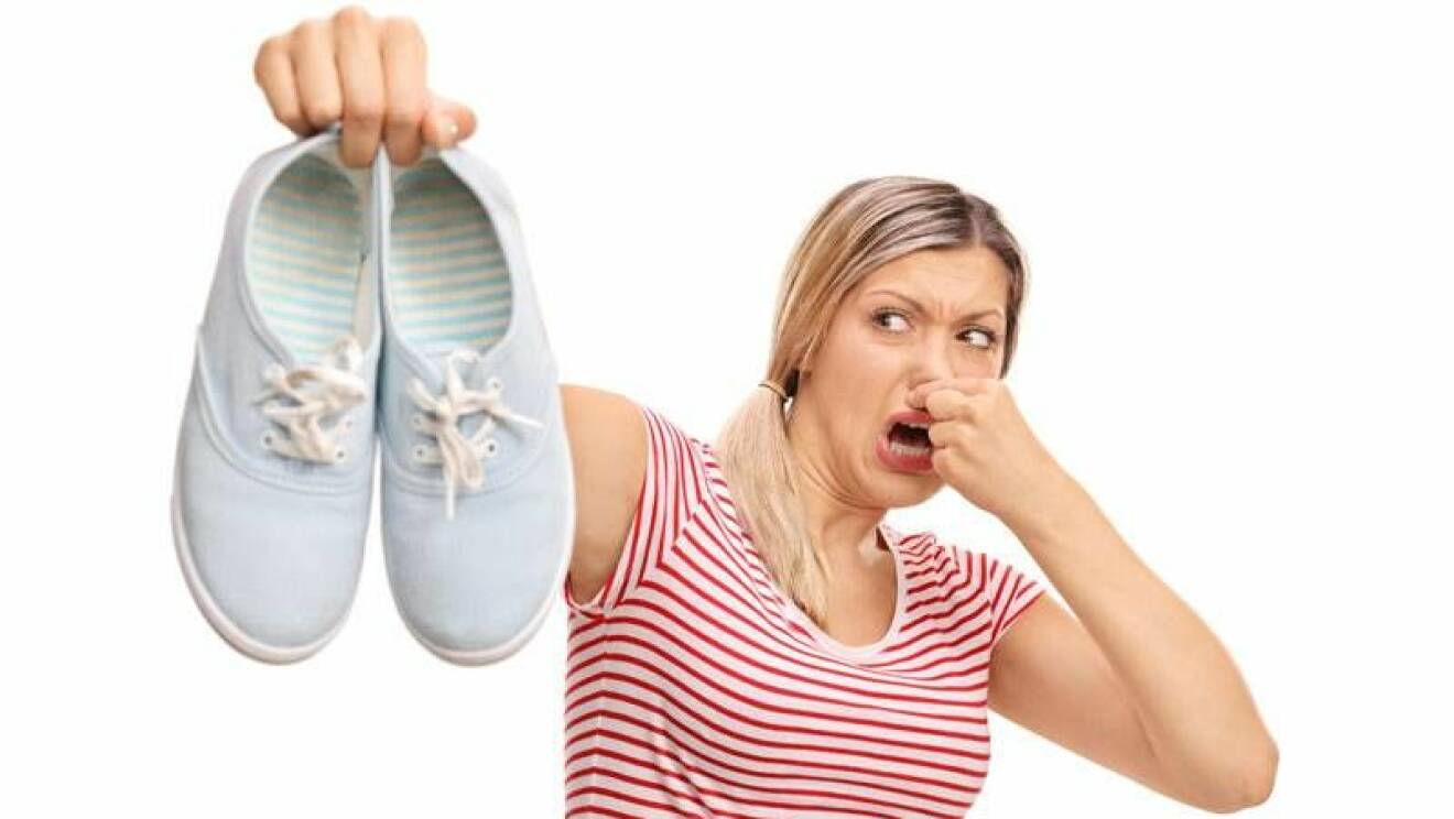 Kvinna som håller upp illaluktande skor och håller för näsan