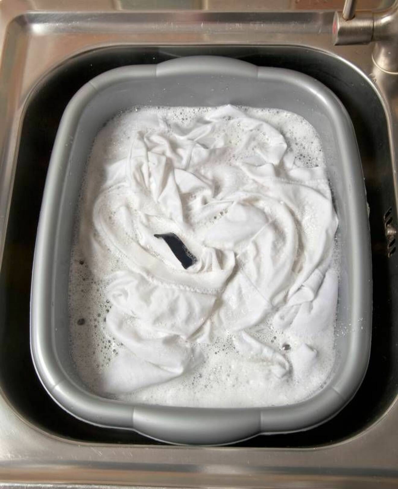 Vita klädesplagg bleks i en balja i vasken