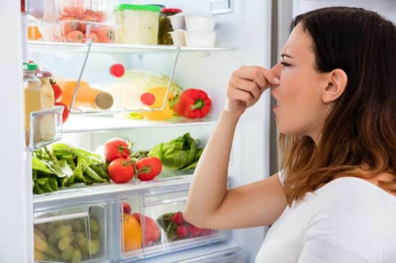 Kvinna håller för näsan när hon tittar in i kylskåpet