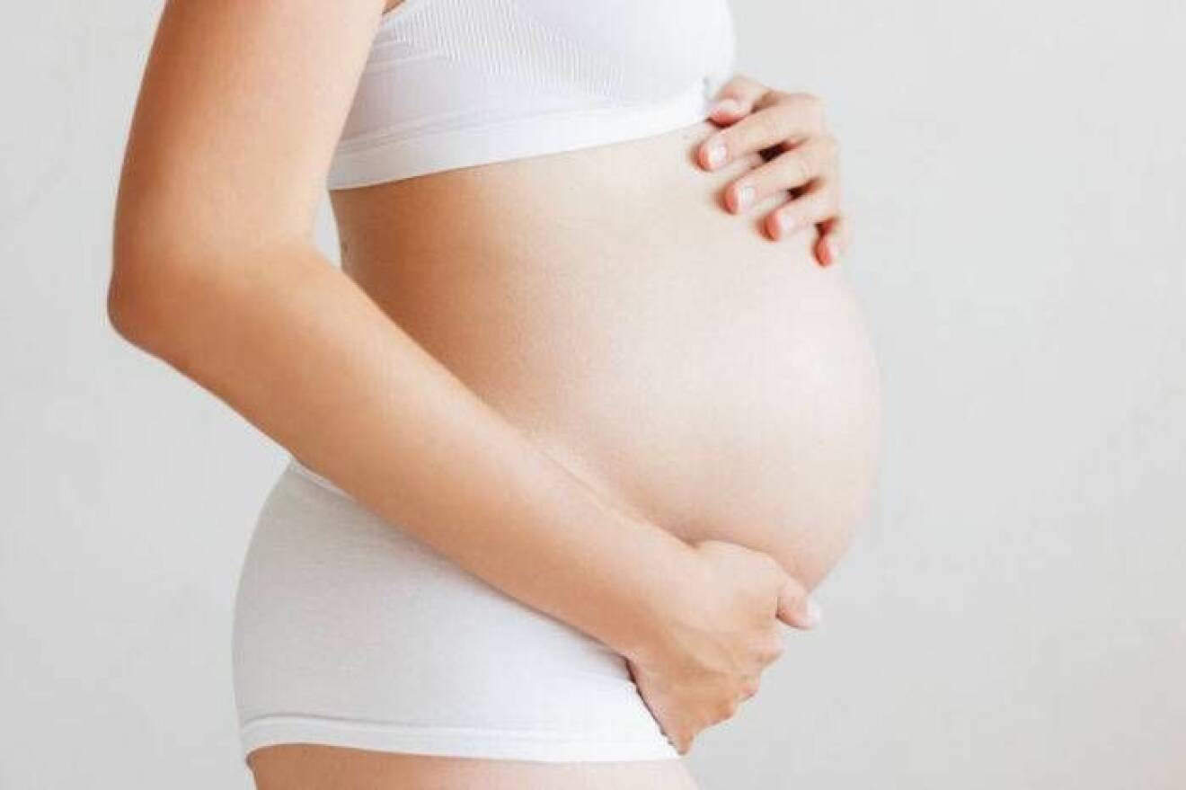 En gravid kvinna i underkläder håller om sin mage