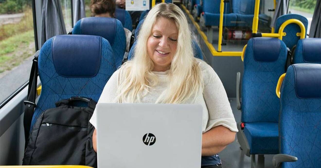 Författaren Anna Ihrén sitter på en buss och tittar ner i sin laptop.