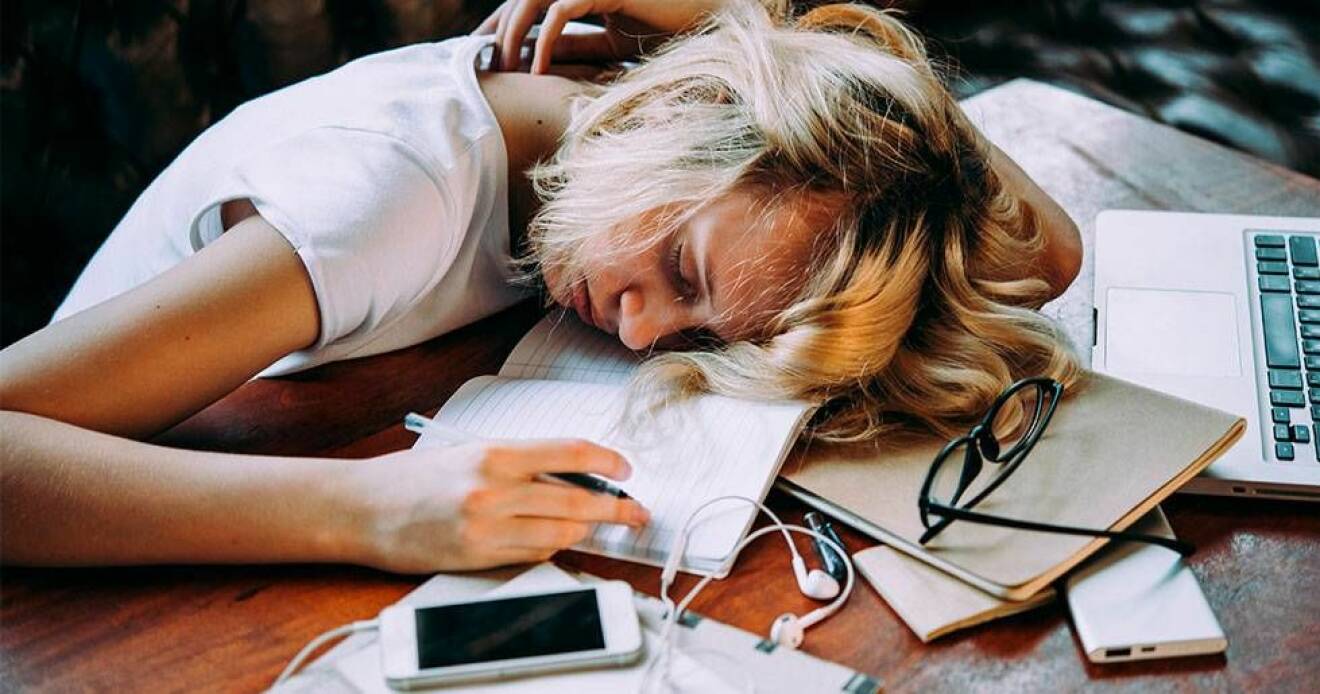 En trött tonårstjej sover på en hög böcker.