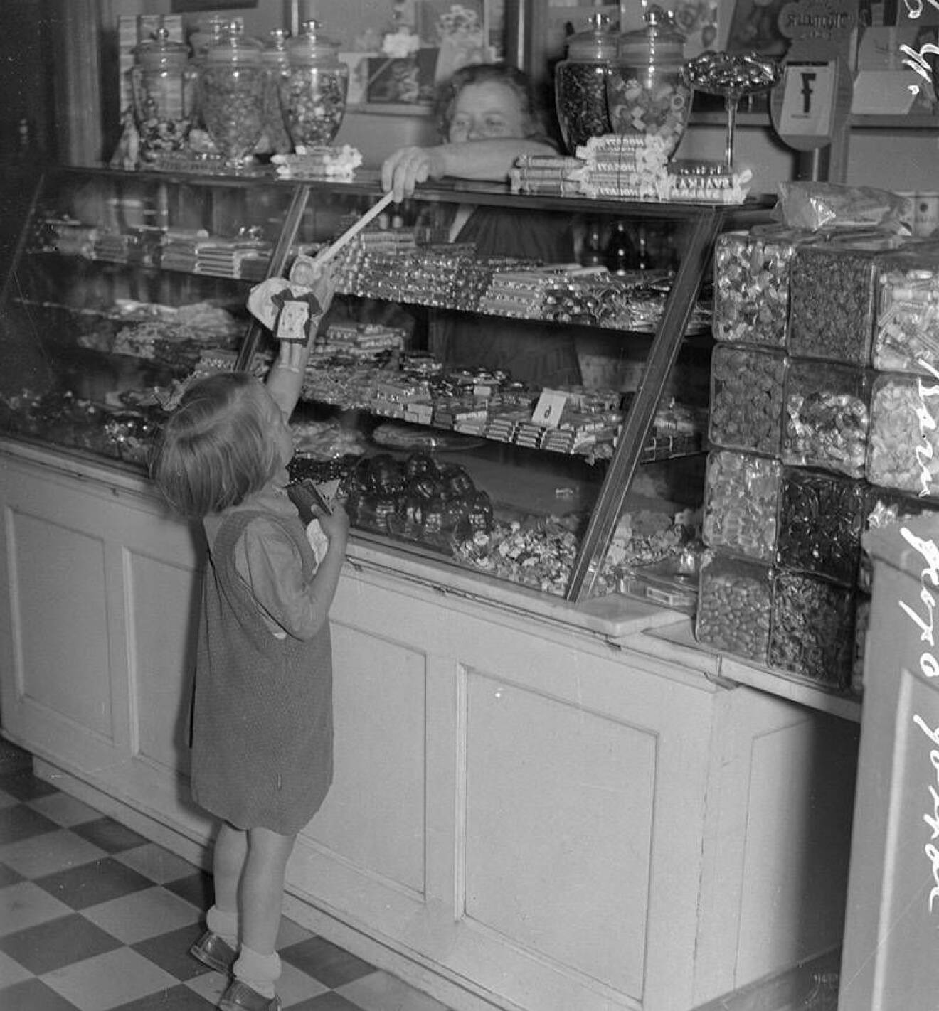 Svartvit bild på en liten flicka som köper godis i lösvikt
