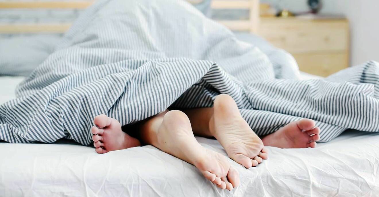Två par fötter sticker ut under ett täcke.