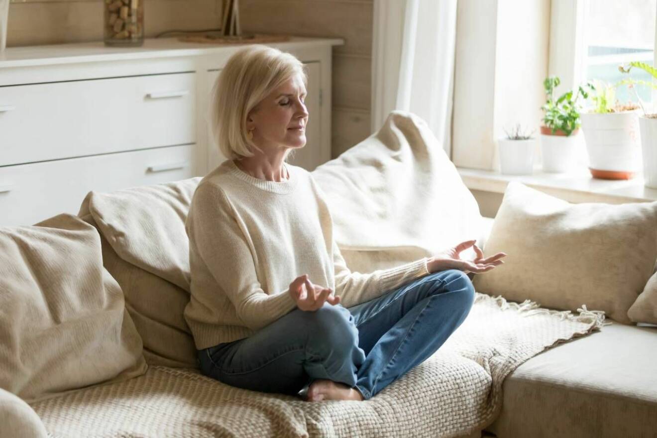 Medelålders kvinna mediterar i soffan