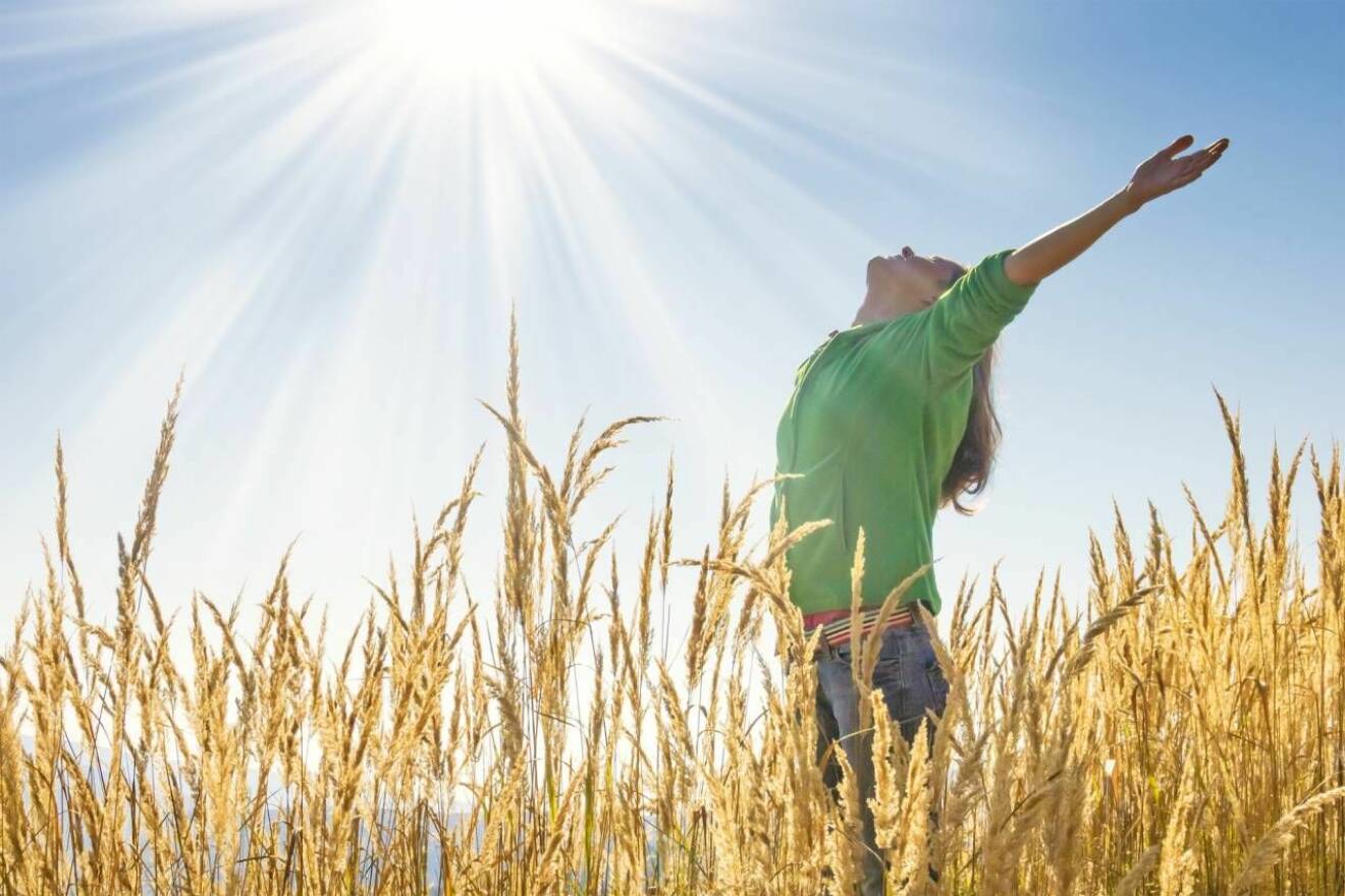 Kvinna på fält vänder upp huvudet mot solen 