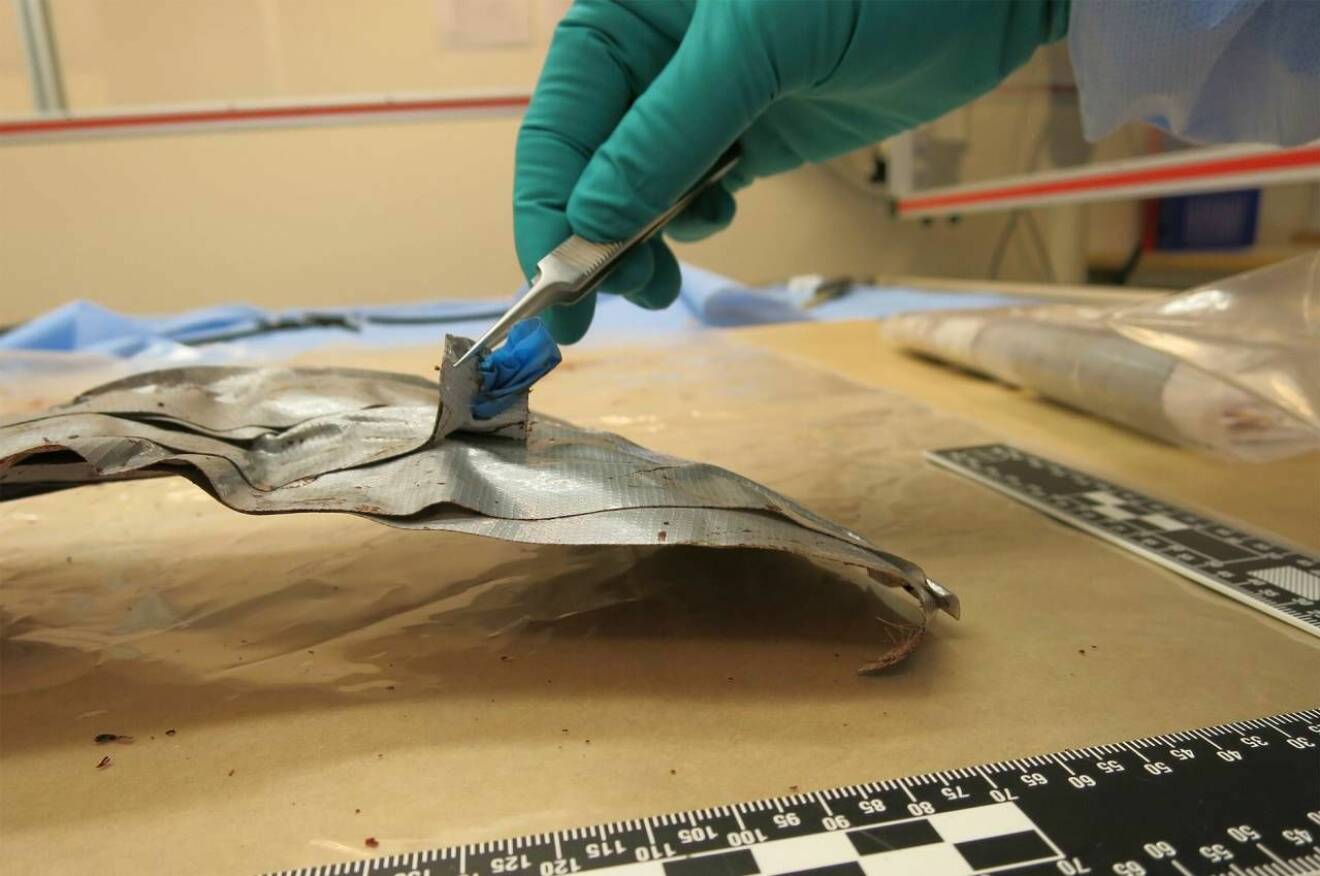 En kriminaltekniker använder pincett för att undersöka en blå plastbit på silvertejp.