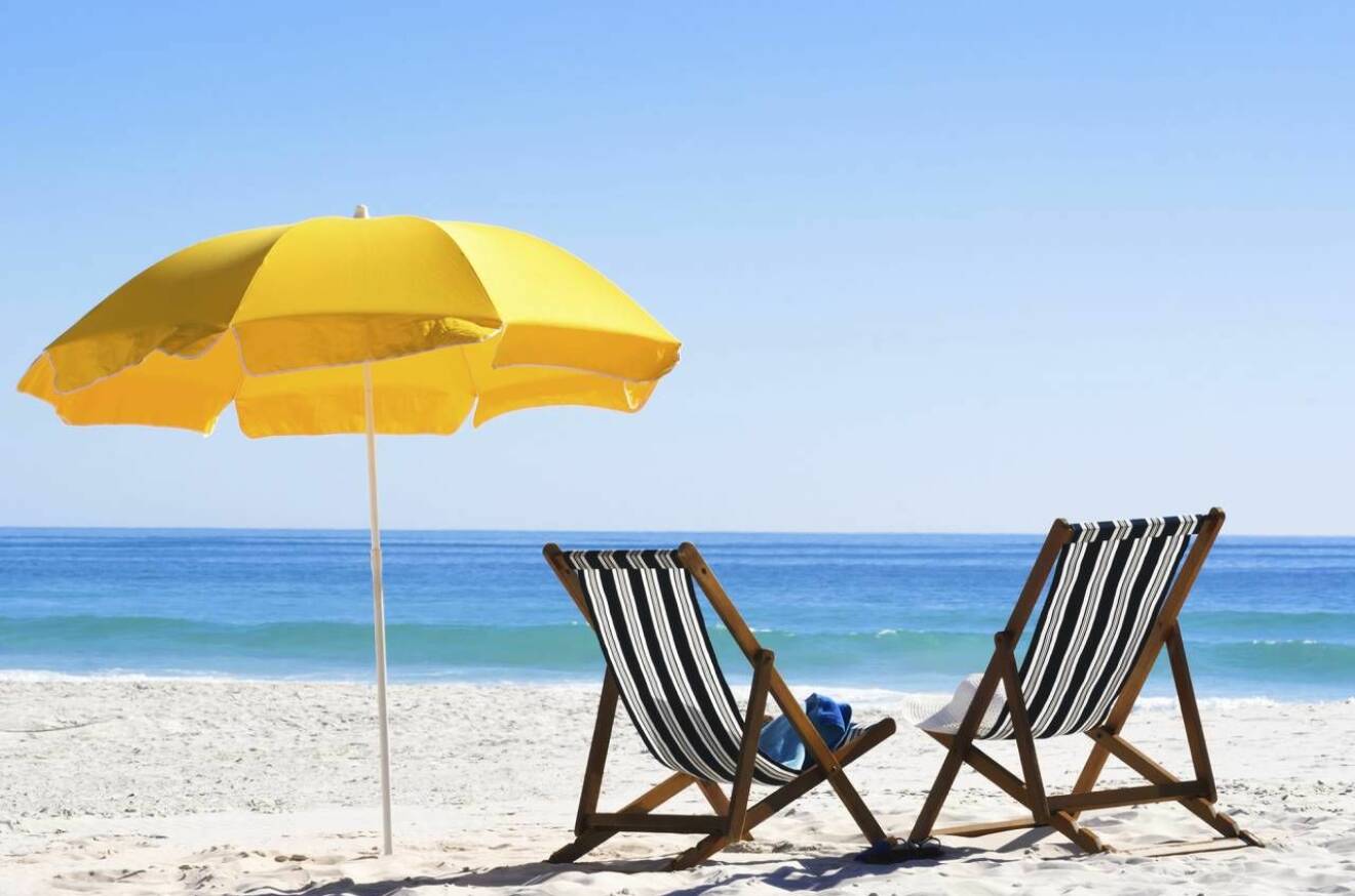 Två solstolar och ett gult parasoll på en strand