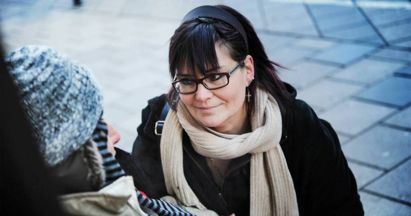 Maria Brändström med mörkt hår och glasögon sitter mittemot en tiggande romsk kvinna.