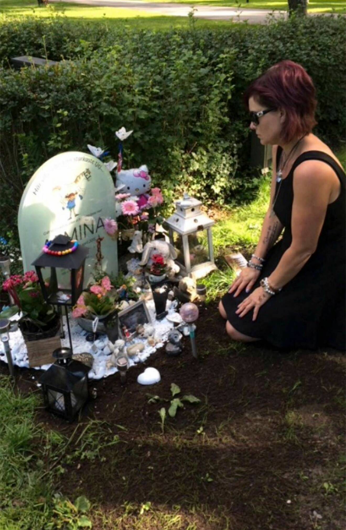 En kvinna sitter på knä framför ett barns grav, pyntad med leksaker och blommor.