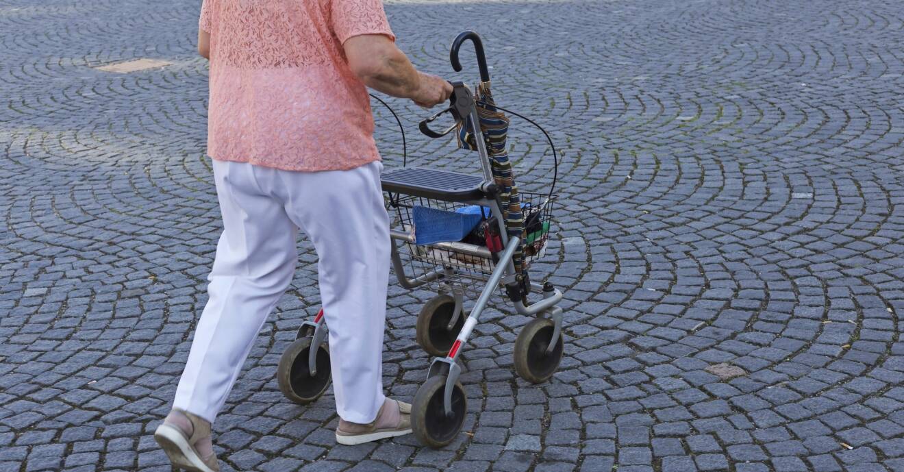 En äldre dam går utomhus med en rullator.