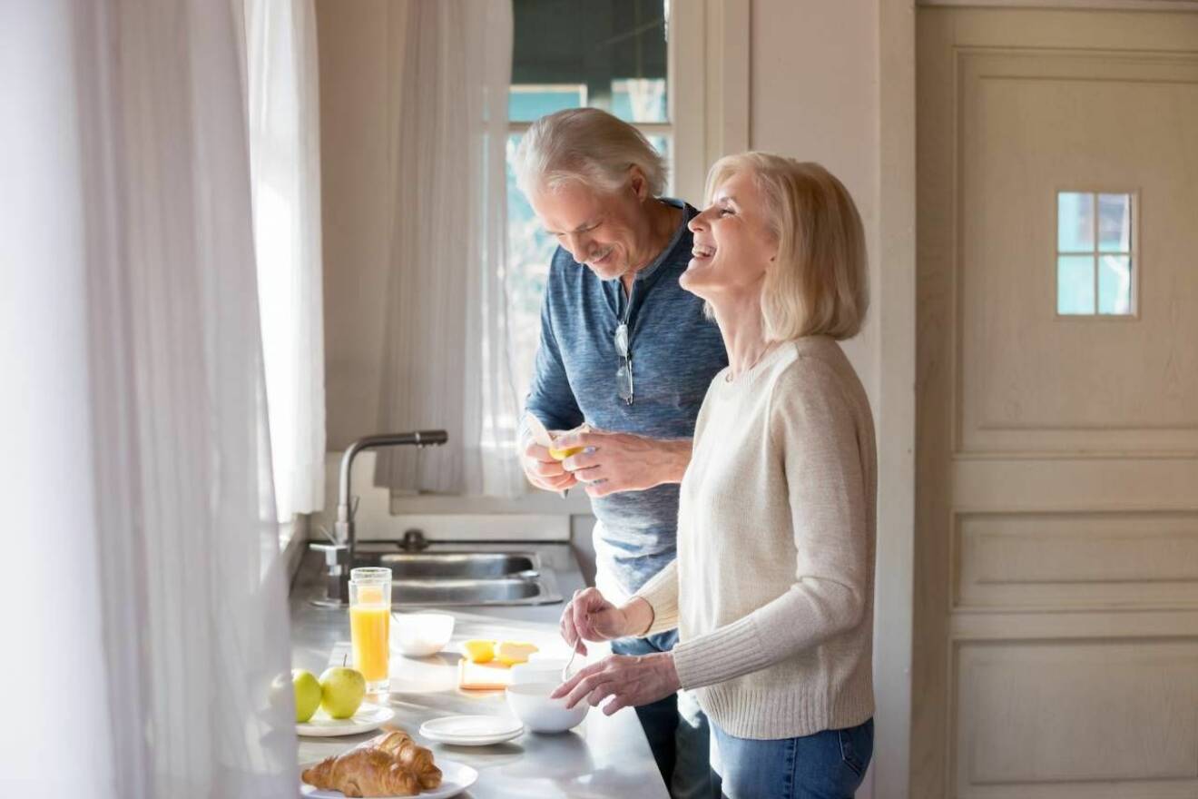 Man och kvinna skrattar och lagar frukost tillsammans. 
