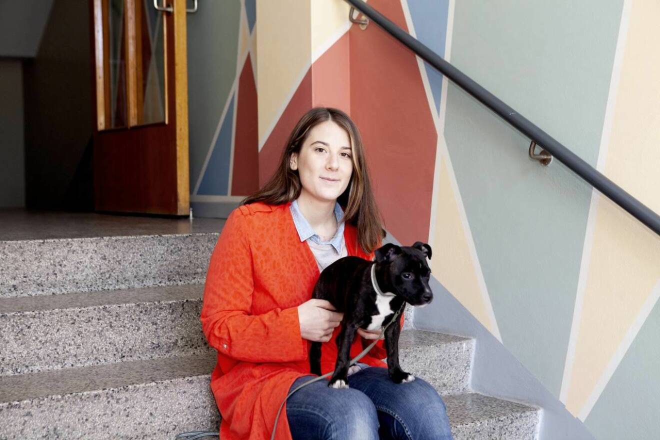 Isabella med sin hundvalp Penny på en yttertrappa med färgglad väggmålning i bakgrunden. 