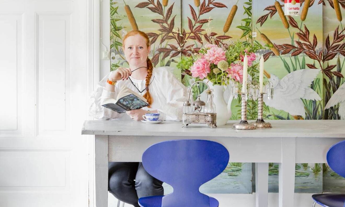 Maria Granström sitter vid ett bord med färgglad tapet i bakgrunden 