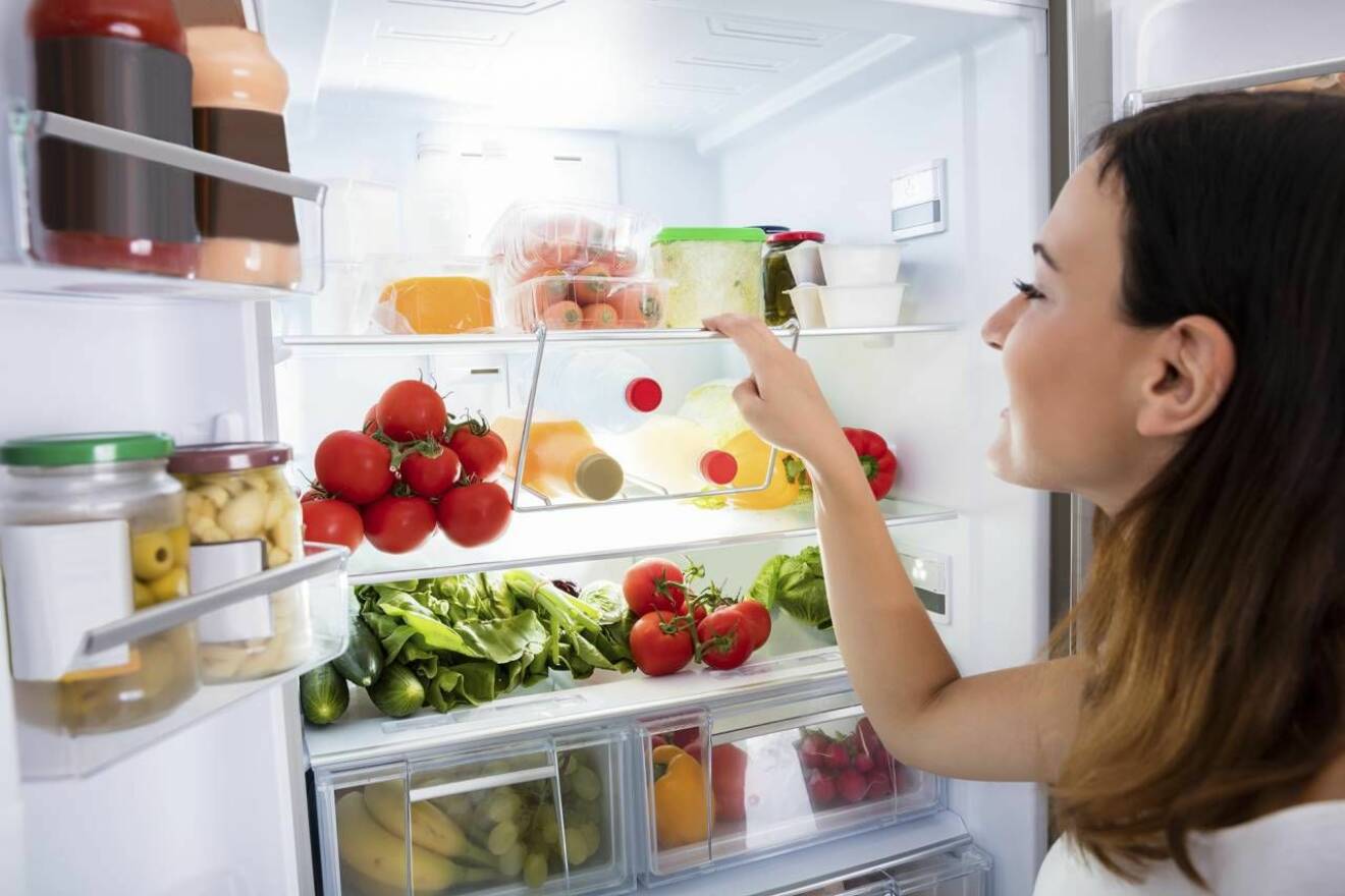 Kvinna tittar på mat i ett kylskåp. 