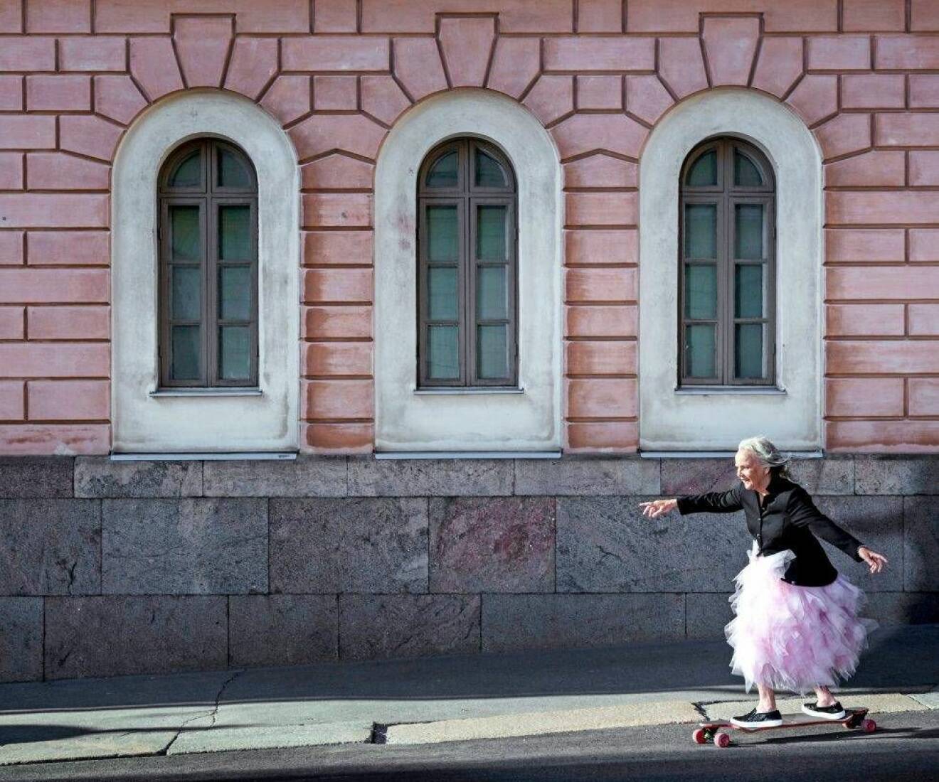 Lena Salmi på longboard framför rosa byggnad.