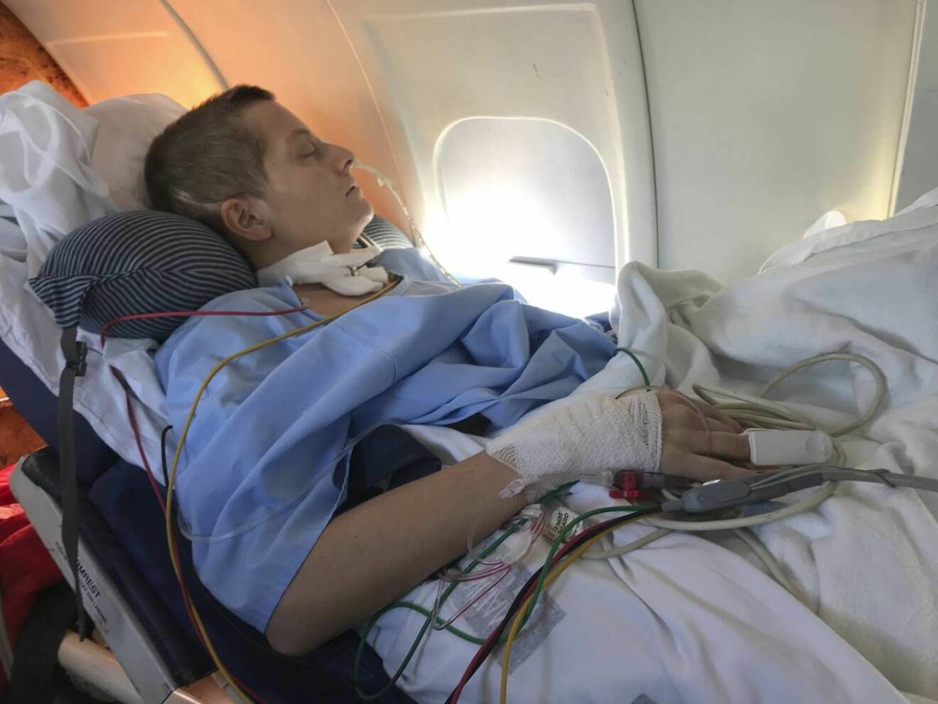 Stina ligger nerbäddad i en sjukhussäng under flygningen hem från Spanien. 