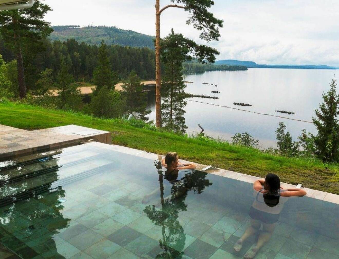 En blank pool utomhus med två personer som blickar ut över den blanka sjön Ljusnan.