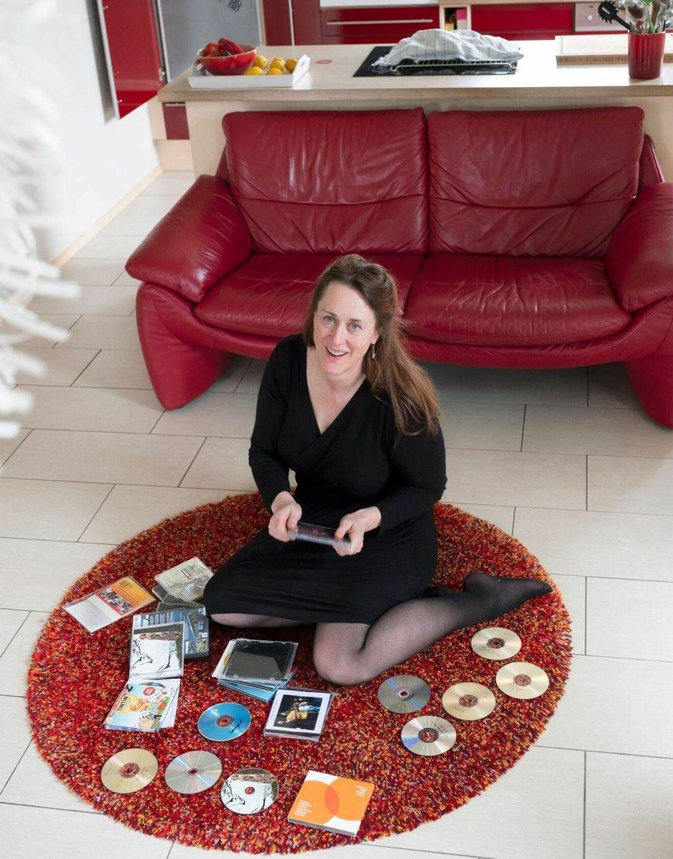 En medelålders kvinna med brunt hår sitter på en matta med cd-skivor utspridda kring sig.