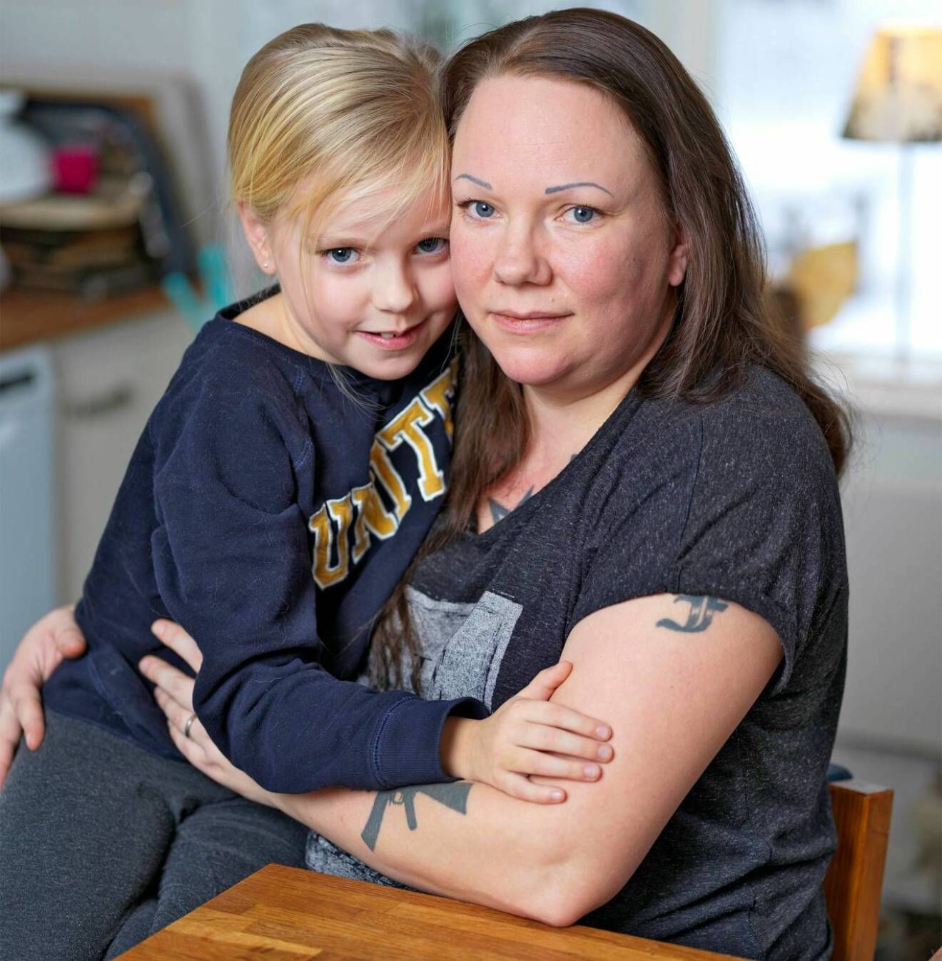 En ung kvinna med tatueringar sitter med sin dotter i knät.