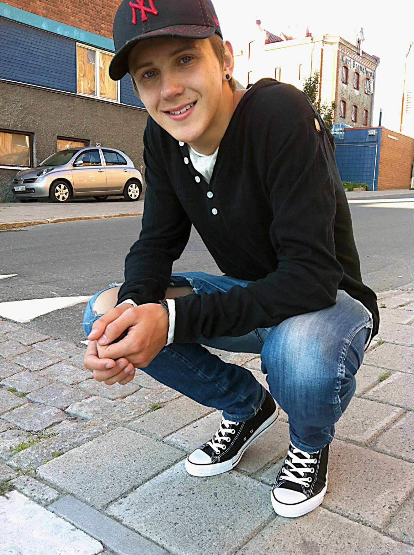 Gustav sitter på huk på en trottoar och ler mot kameran. 