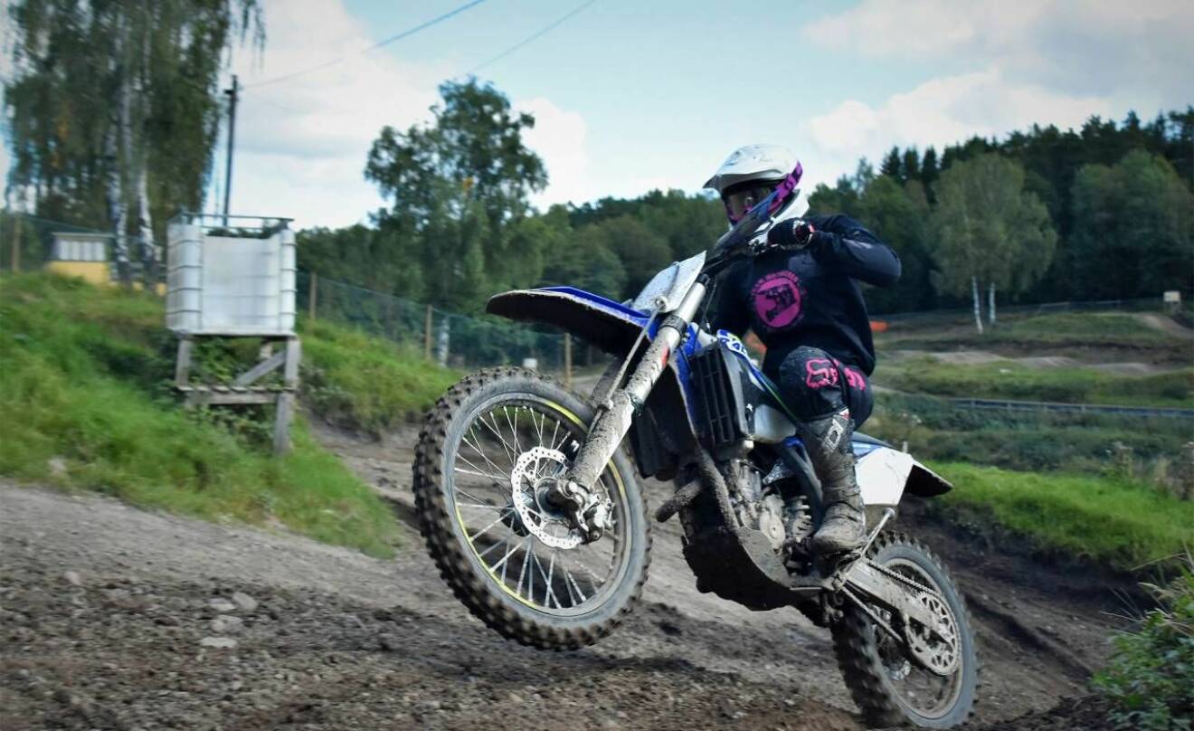 En kvinna kör motocross uppför en lerig backe.