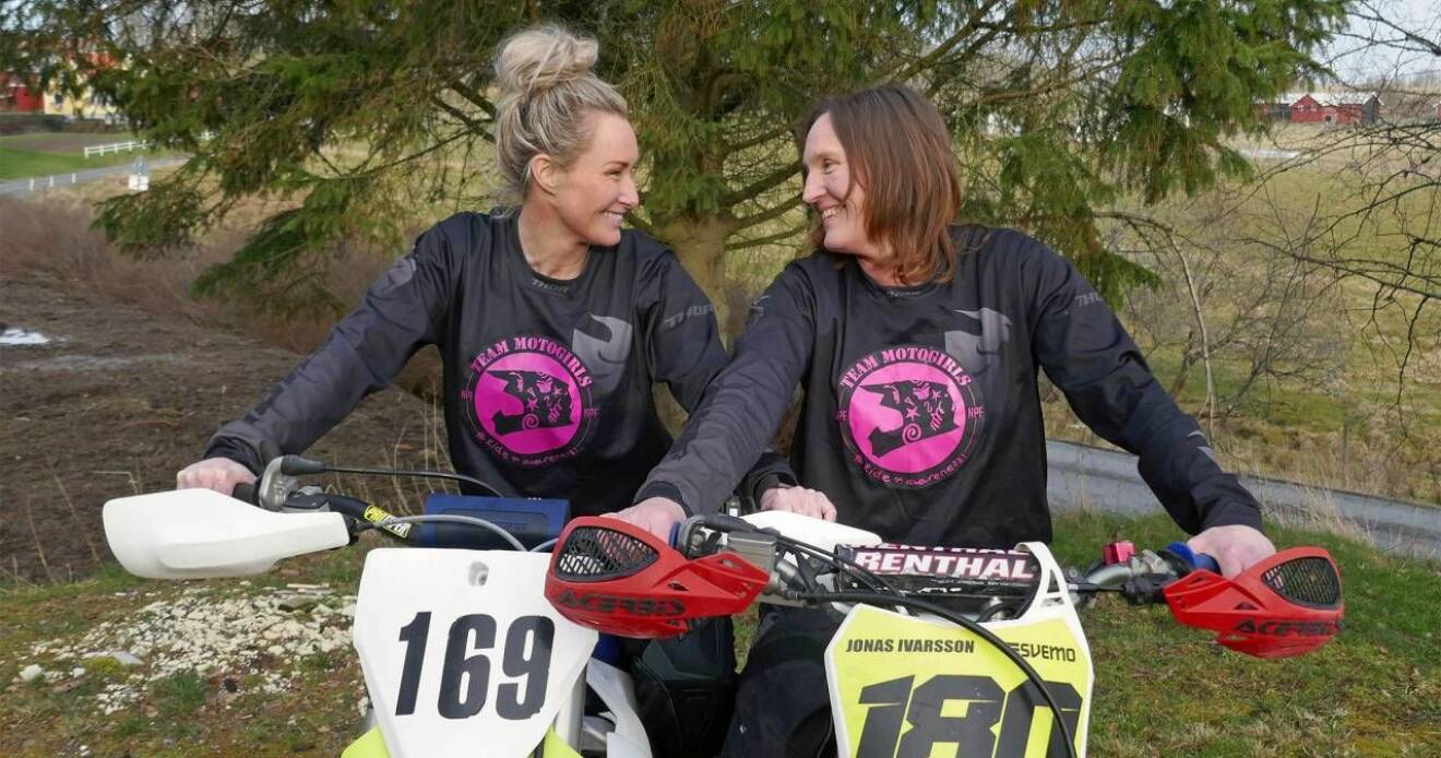 Två kvinnor sitter på varsin motocross-cykel, ler och tittar på varandra.
