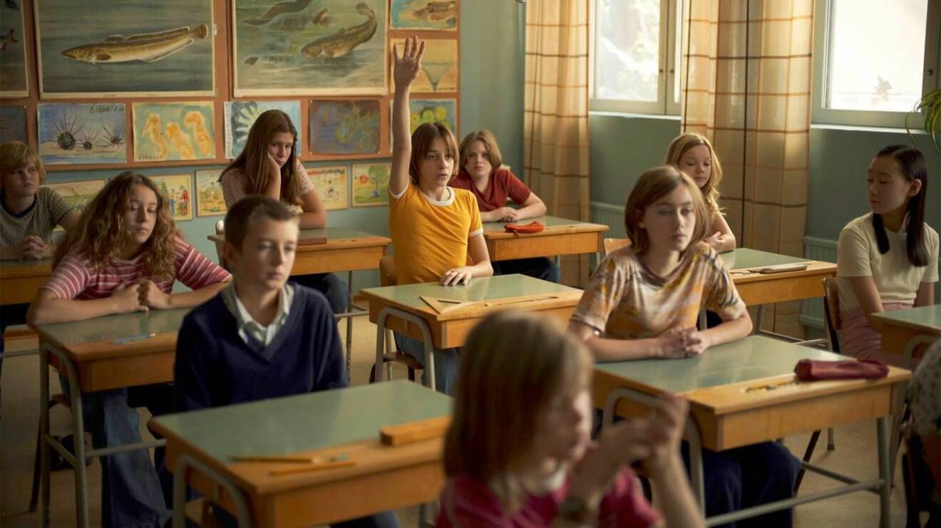 Bild från ett klassrum ur filmen En komikers uppväxt, huvudkaraktären Juha räcker upp handen.