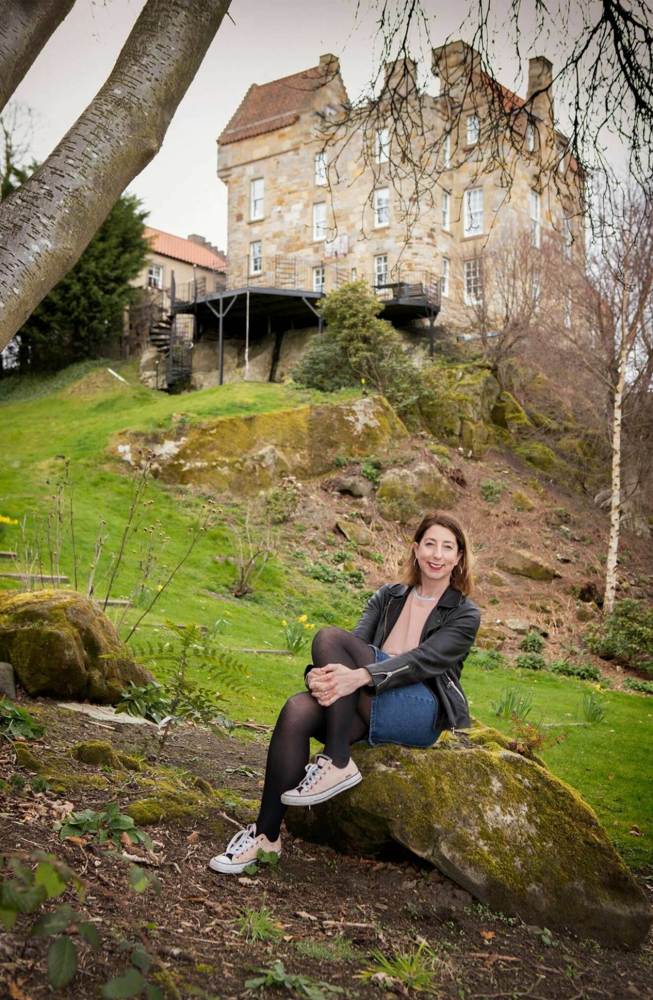Författaren Jenny Colgan sitter framför ett slott i Skottland där hon bor med sin familj.